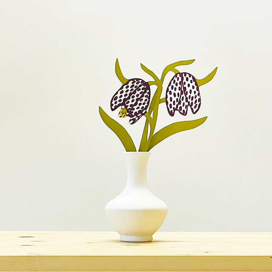 Decorative wooden flowers in a white vase on a light wooden surface with a light gray background