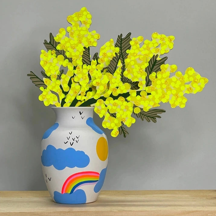 Vase with colorful design and yellow flowers on a wooden surface against a gray background