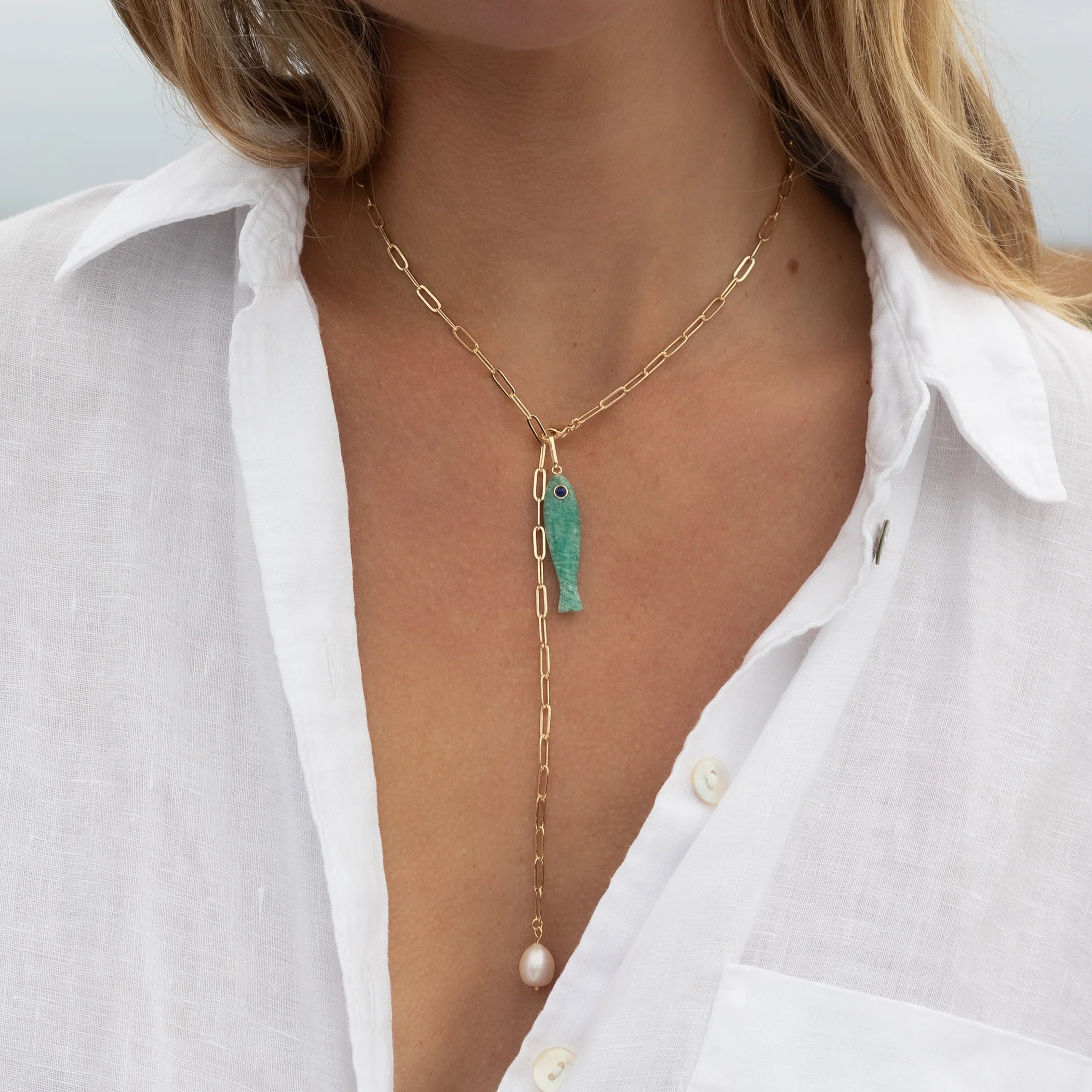 Necklace with a green fish pendant and pearl drop worn by a person in a white shirt.