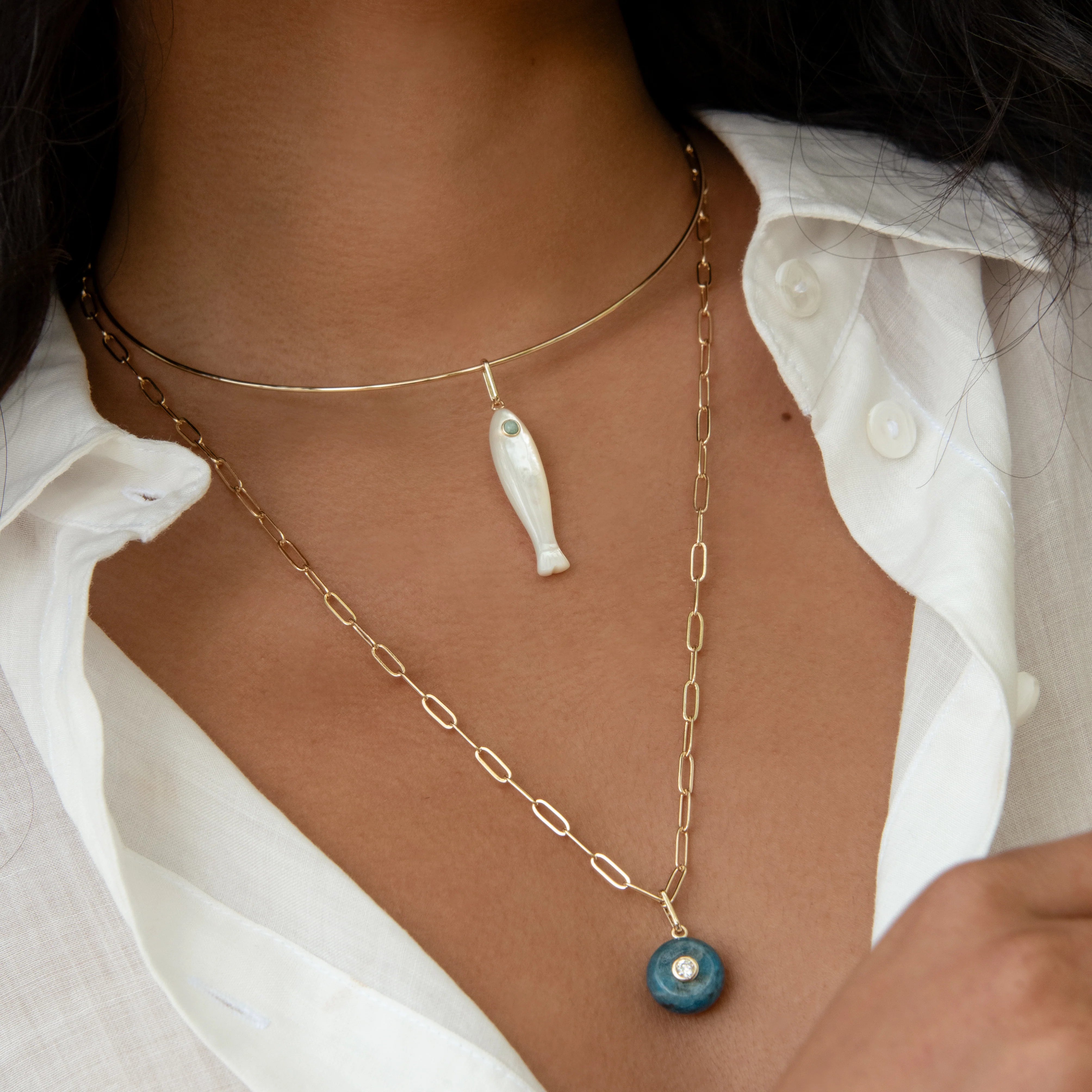 Necklace with fish and blue pendant worn by a person in a white shirt