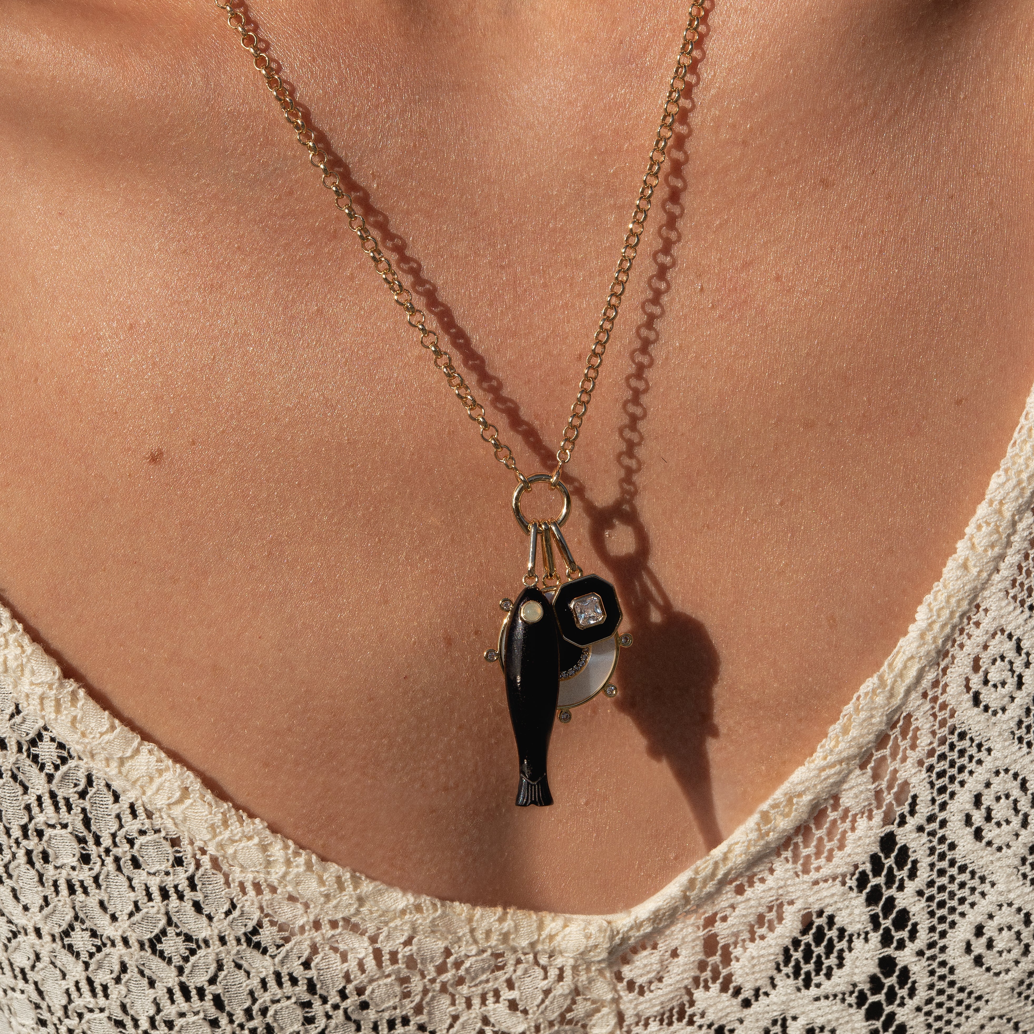 Necklace with a pendant featuring a fish and a wheel on a person wearing a lace top.