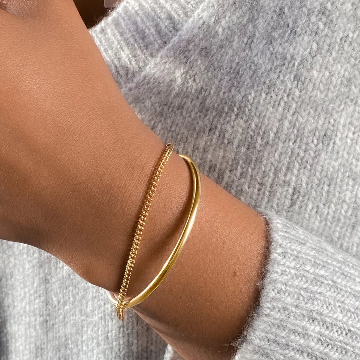 Gold bracelet on a wrist with a gray sweater background
