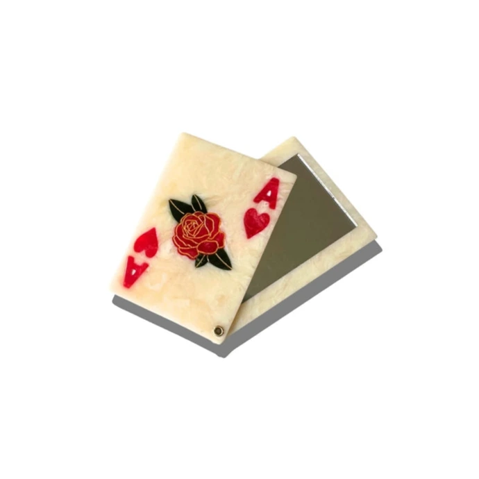 a white and red compact mirror in the shape of a playing card with the detail of the ace of hearts and a floral motif on a white background