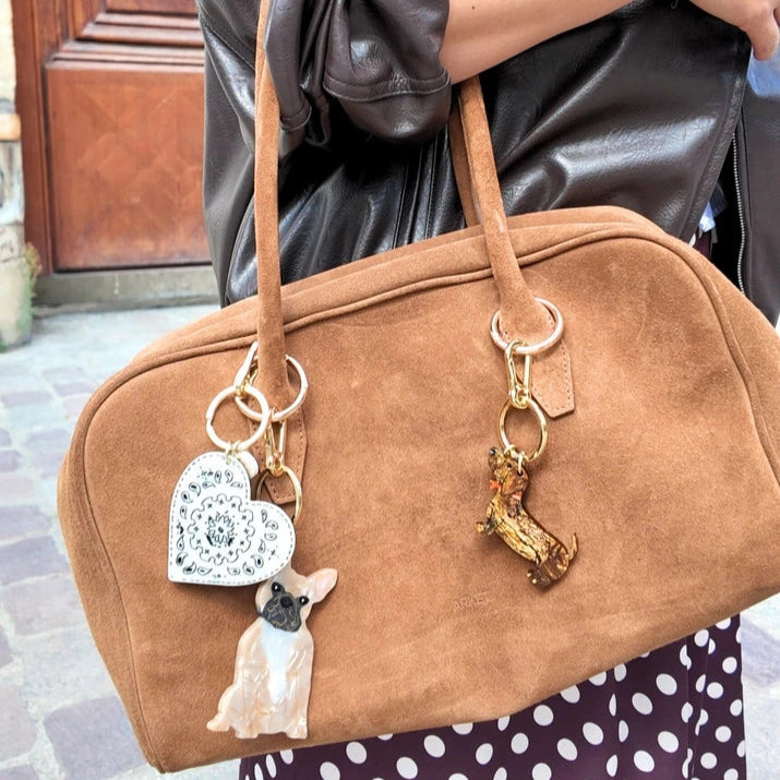 Brown handbag with dog charm held by a person wearing a leather jacket.