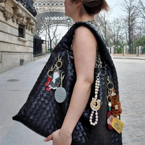 Woman with a large black handbag featuring various accessories in front of the Eiffel Tower.