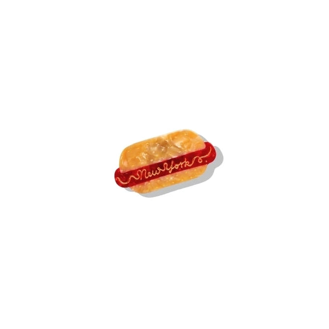 a yellow and red painted brooch in the shape of a hotdog with text reading new york in mustard on a white background