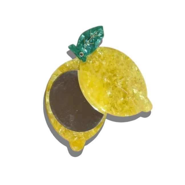 Compact mirror shaped like a lemon with a green leaf on a white background