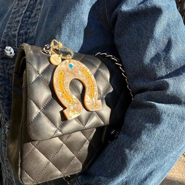 Gray quilted handbag with a horseshoe charm held by a person wearing blue jeans.