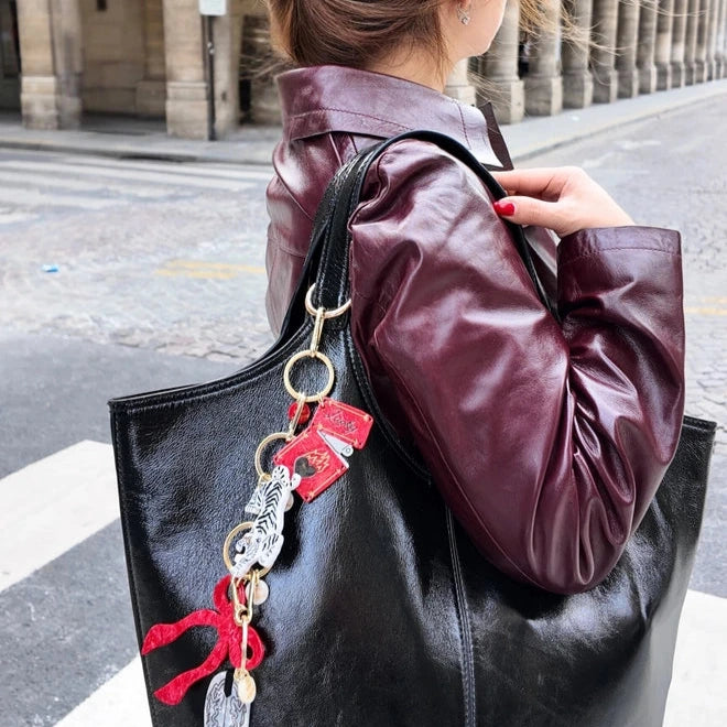 A person standing on a city corner with a black handbag that has several keychains attached