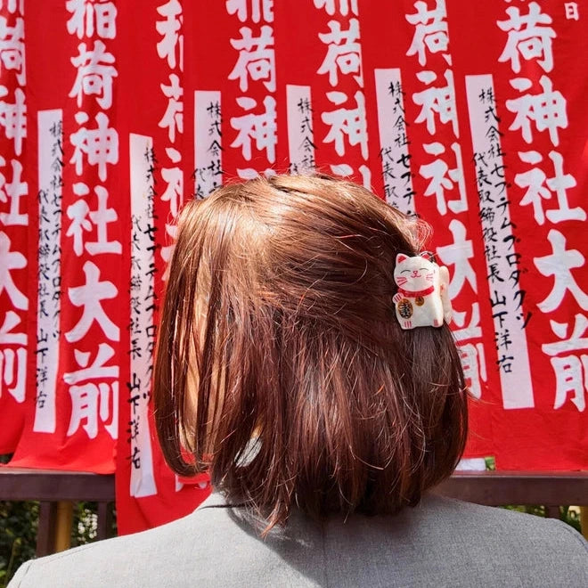 Person with a hair clip featuring a small cat figurine in front of red banners with white text.