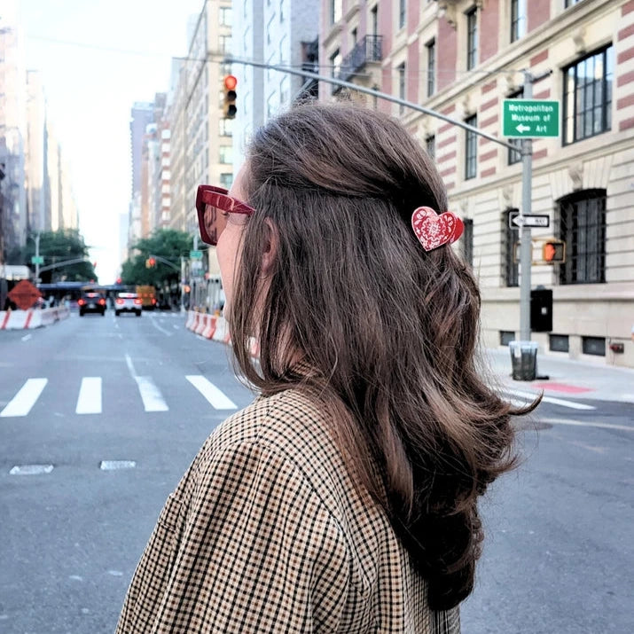 Person with styled hair and a red heart shaped claw clip on a city street