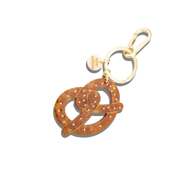 A brown pretzel keychain with white polka dots with a gold clasp with a white background