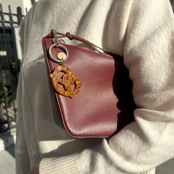 Person holding a maroon handbag with a decorative keychain in an outdoor setting