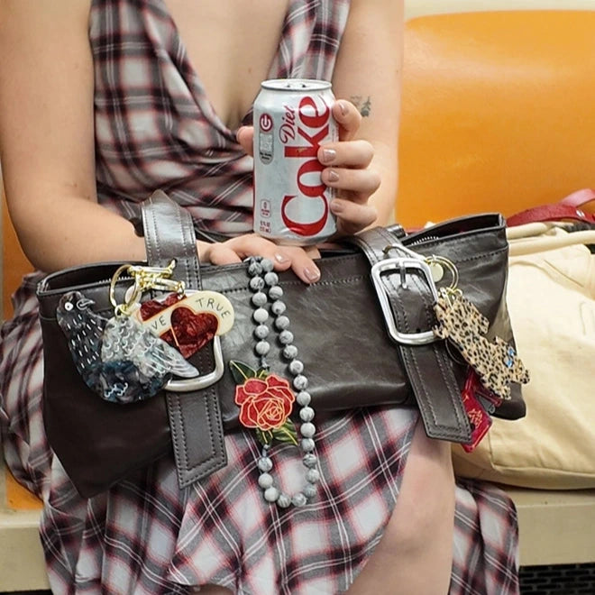 Person holding a can of Diet Coke with a decorated handbag on a subway train.
