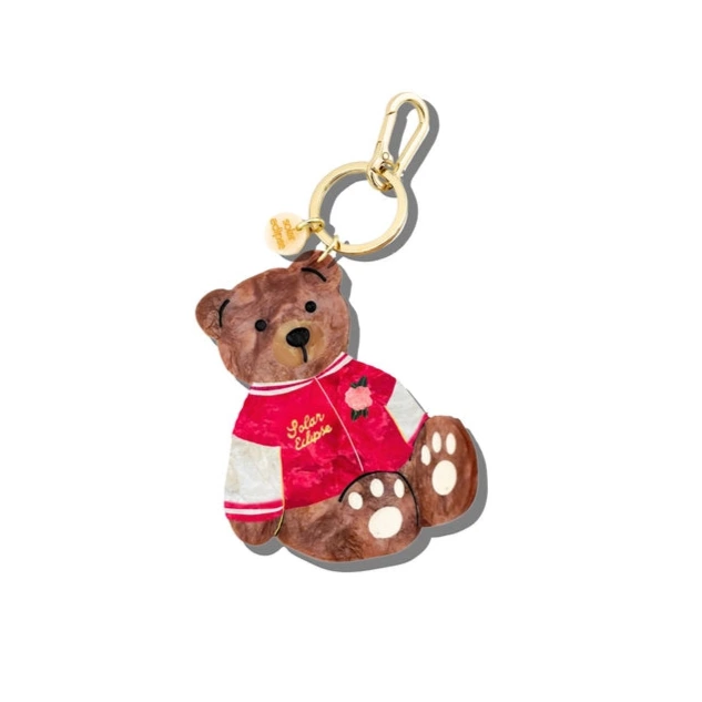 A keychain of a bear in a red and white varsity jacket with a gold clasp on a white background 