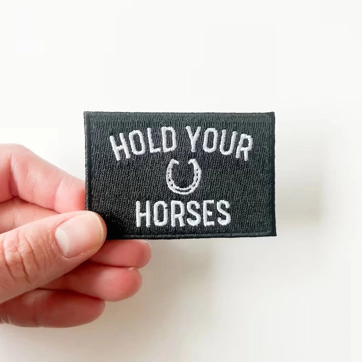 a black and white patch with text reading hold your horses on a white background