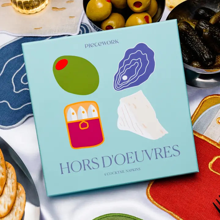 a blue box containing linen cocktail napkins with a white tablecloth background and surrounded by napkins and hors d'oeuvres