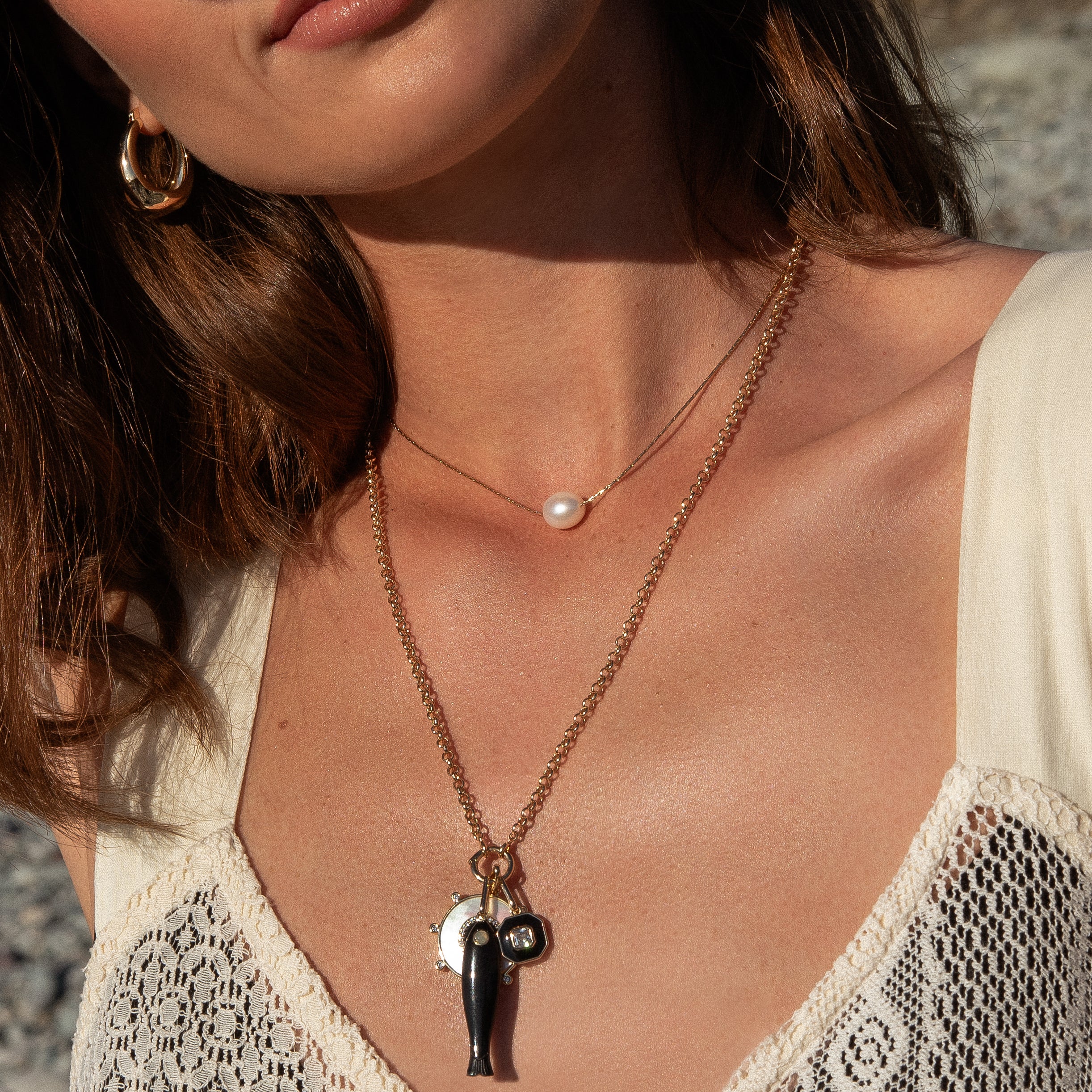 a woman wearing several gold necklaces including a gold chain with a large oval pearl over a white blouse