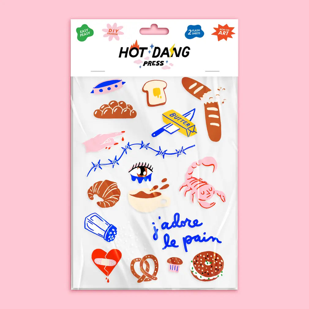 A package of Hot 'Dang Press temporary tattoos featuring various French bakery and food illustrations, including croissants, baguettes, pretzels, and a heart that reads 'j'adore le pain', set against a solid pink background.