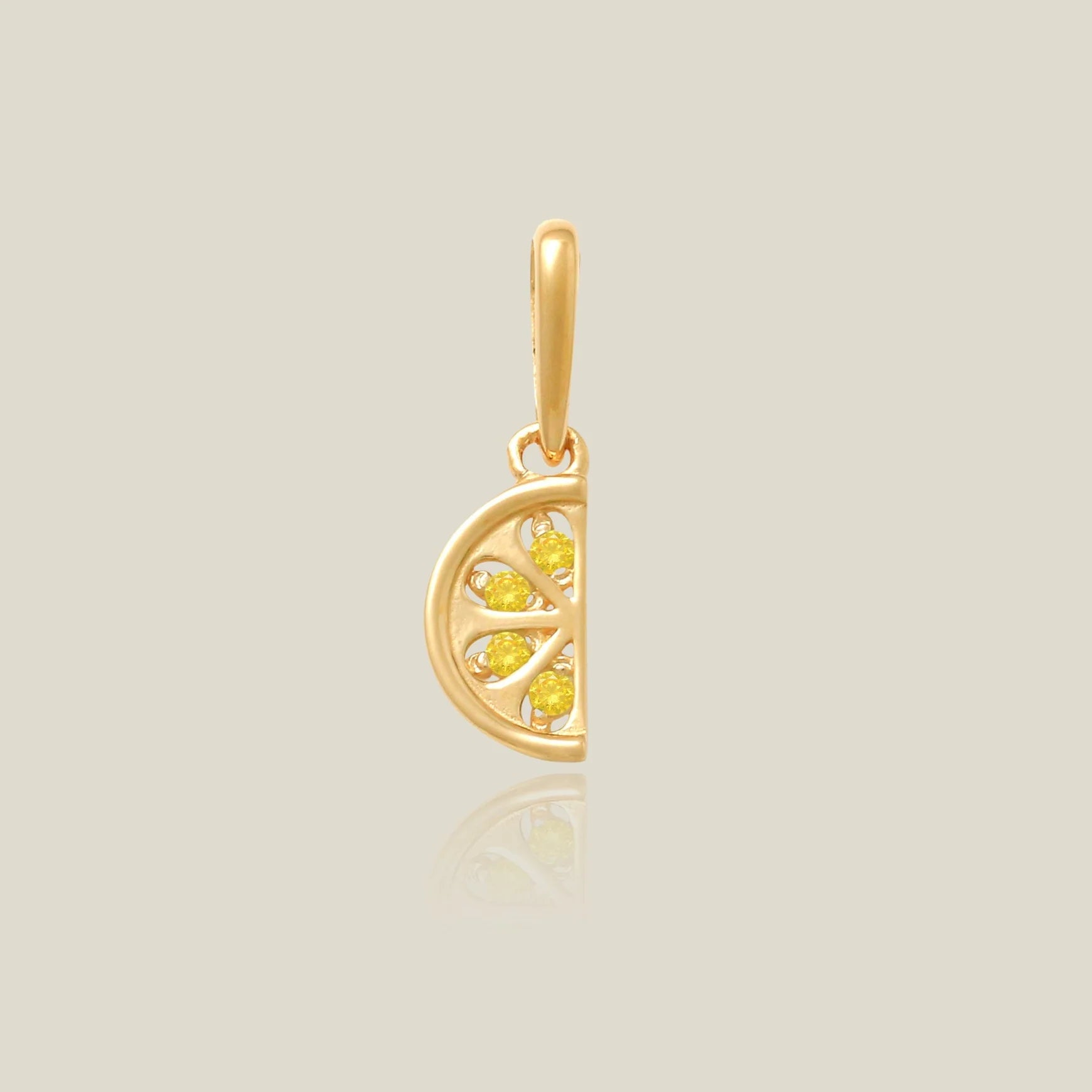 A gold pendant shaped like a lemon slice, featuring three small yellow gemstones, shown on a light beige background with a soft reflection below.