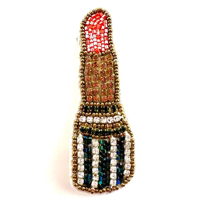 a gold, red, and black brooch in the shape of a stick of lipstick on a white background
