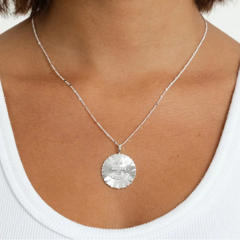 a silver pendant charm on a necklace worn on the neck of a person wearing a white top