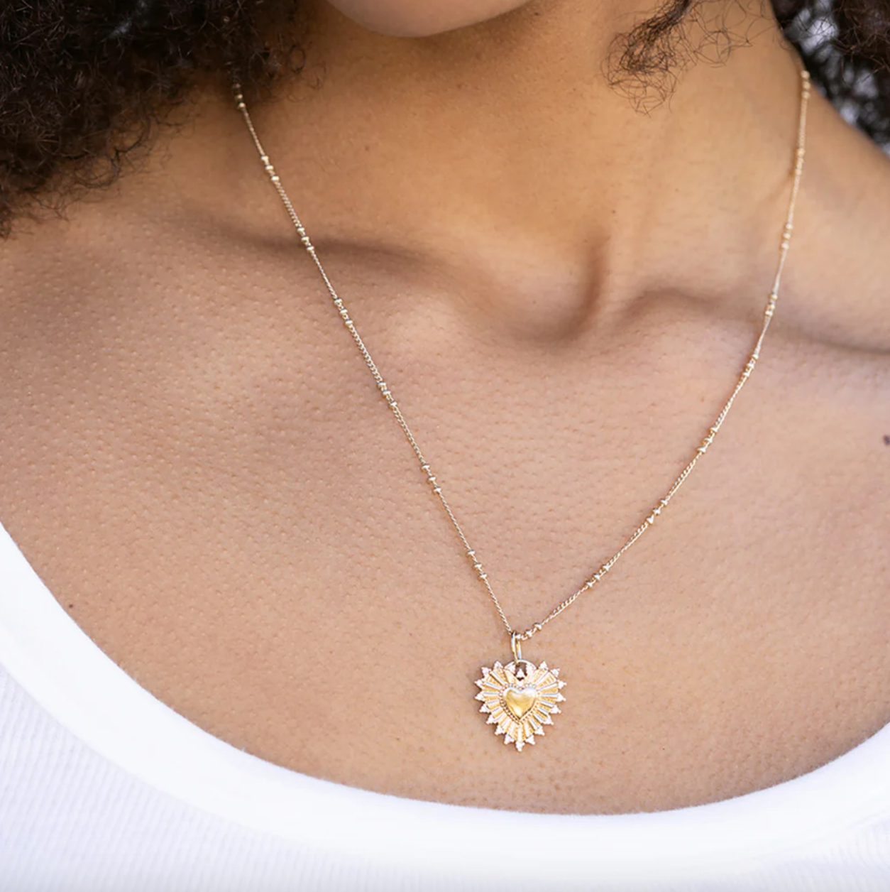 Gold necklace with a heart-shaped pendant worn by a person