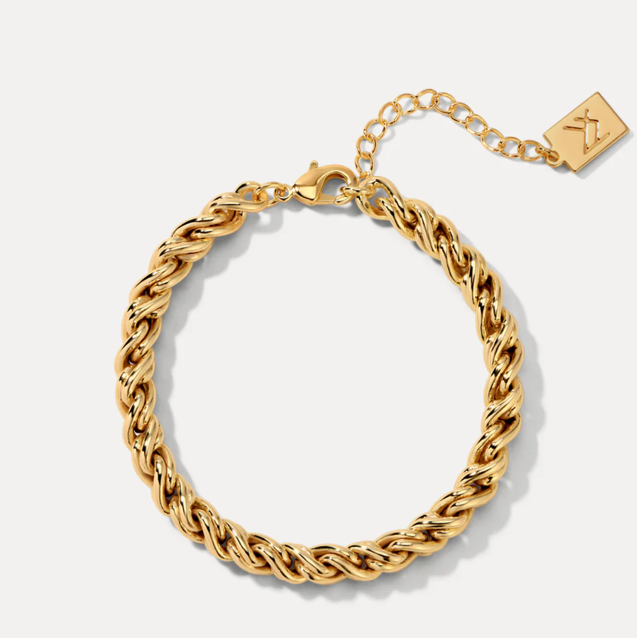 Gold braided bracelet on a white background with a visible brand logo.