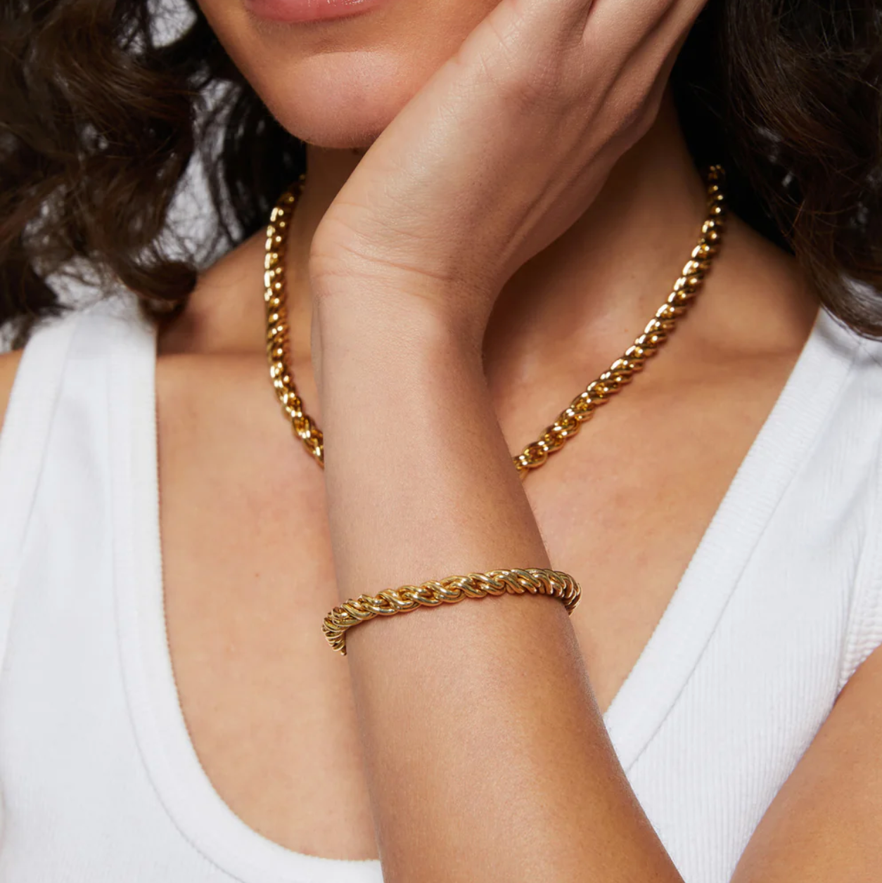 Woman wearing a gold chain necklace and bracelet on a plain background