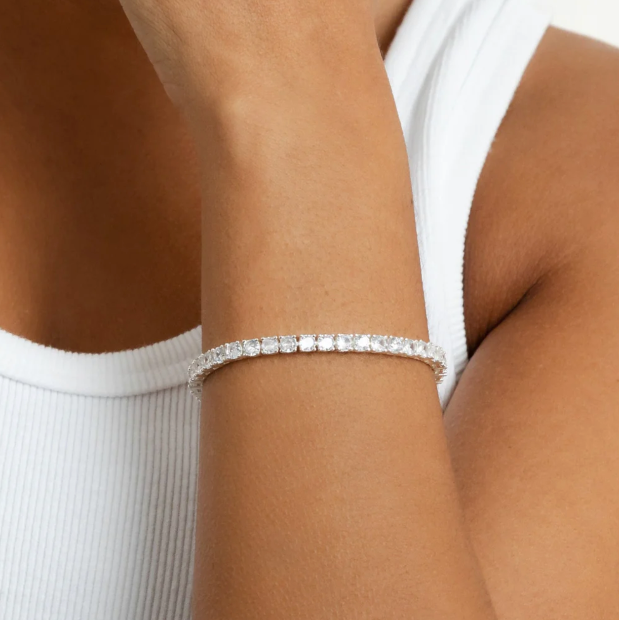 Gold tennis bracelet with CZs on a light gray background on wrist