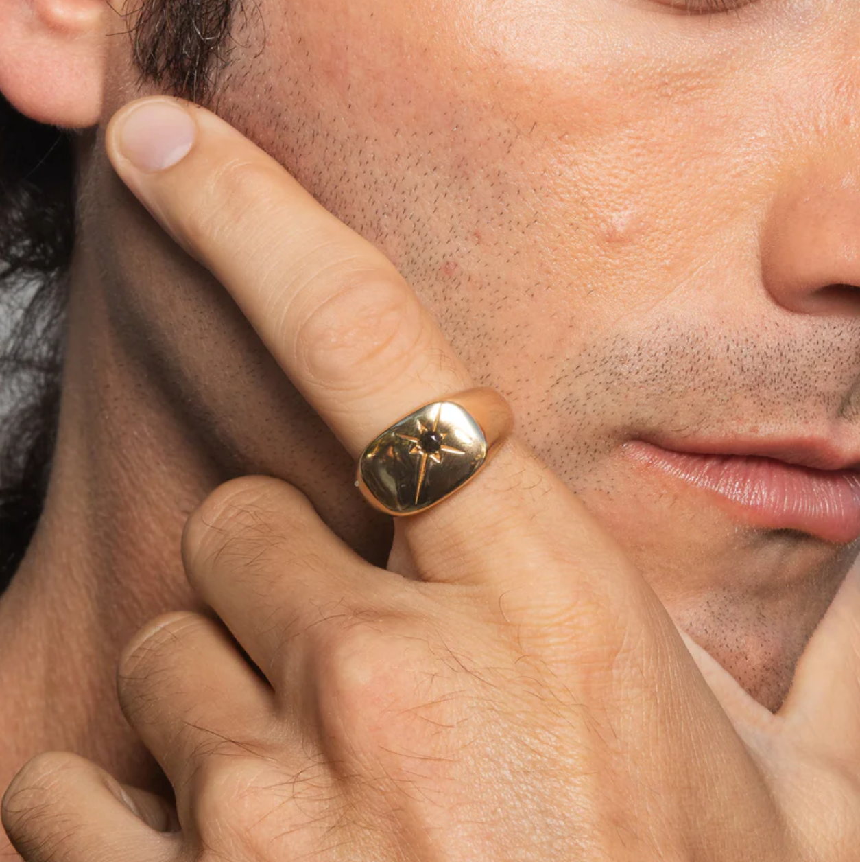 Close-up of a man's hand with a gold ring on his finger, touching his face.
