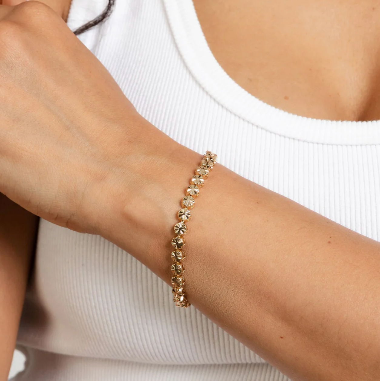 Gold bracelet on a wrist with a white tank top background