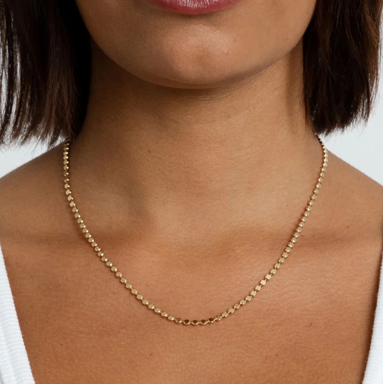 Gold discs necklace on a person with a neutral background