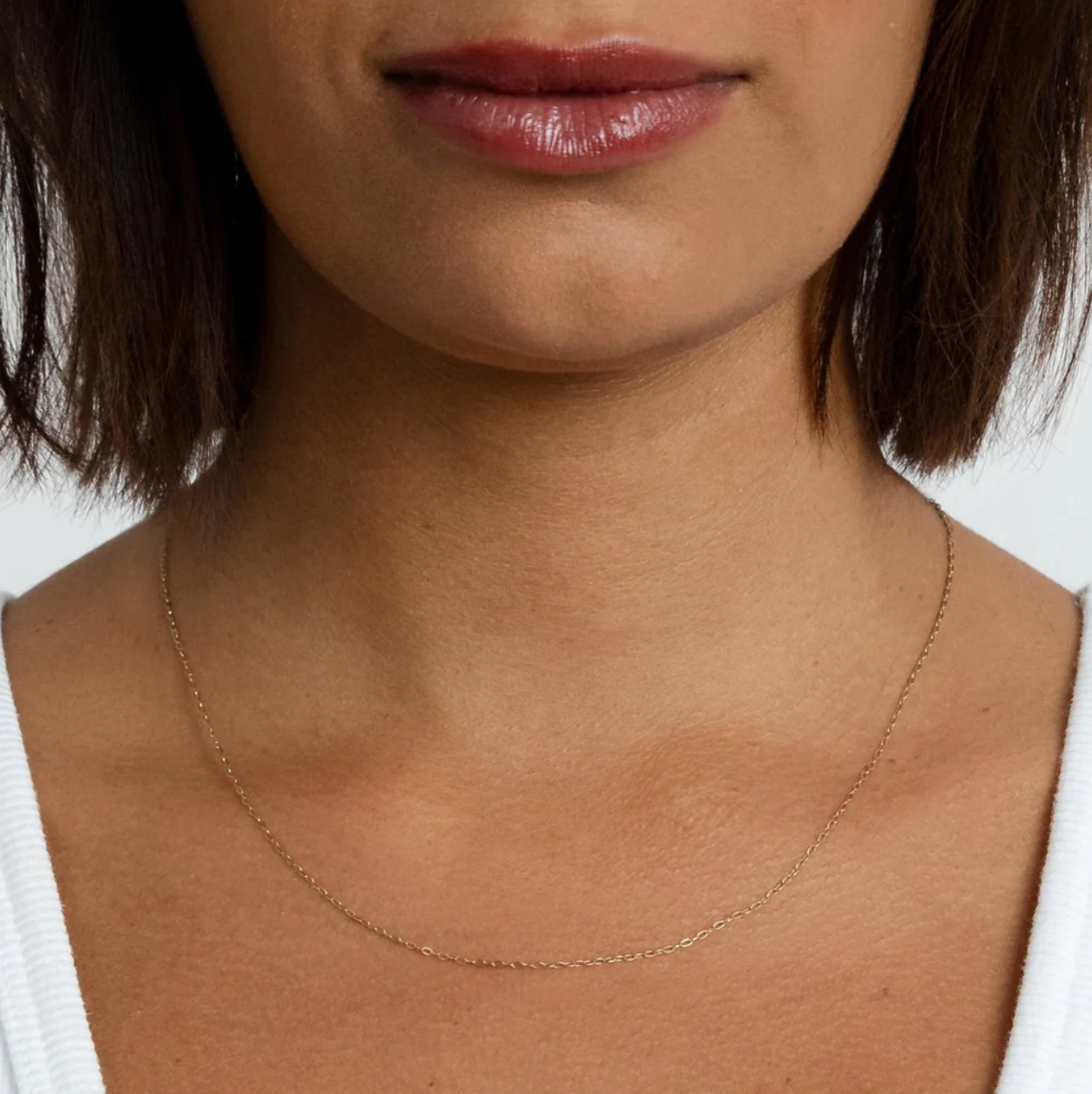 Close-up of a person wearing a delicate gold necklace against a neutral background