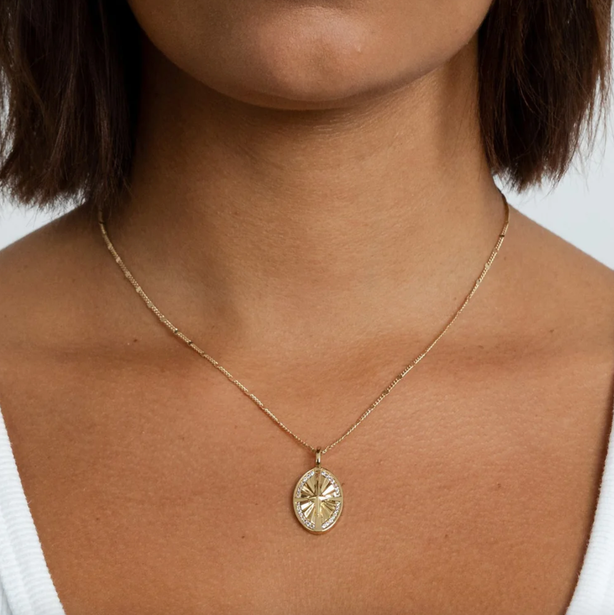 Gold necklace with a pendant on a person against a neutral background