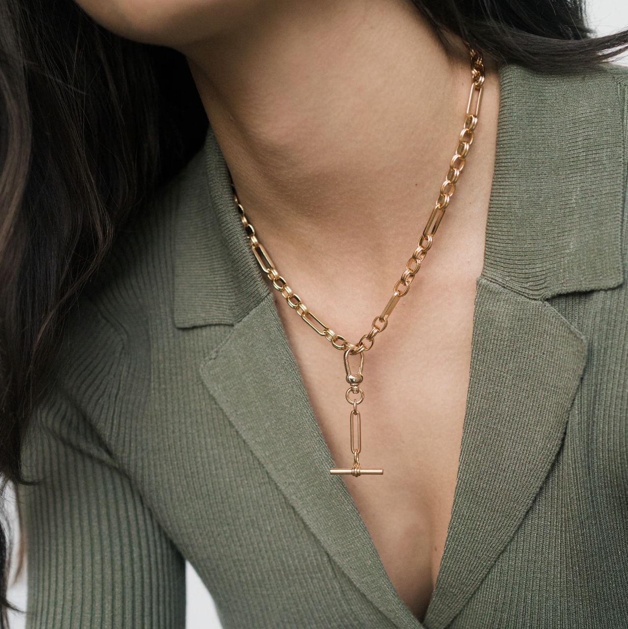 Gold chain necklace with a toggle pendant worn by a person in a green blazer.