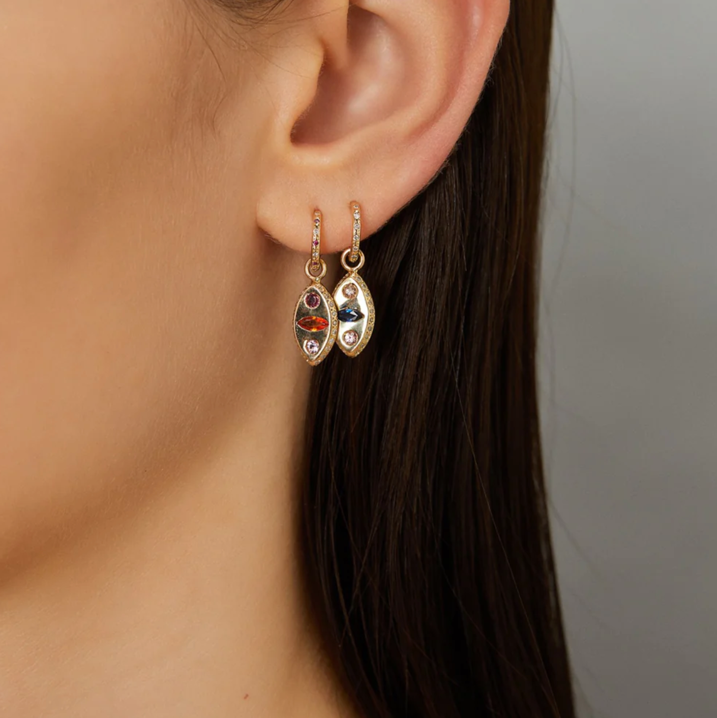 Close-up of a person wearing gold earrings with gemstones against a neutral background
