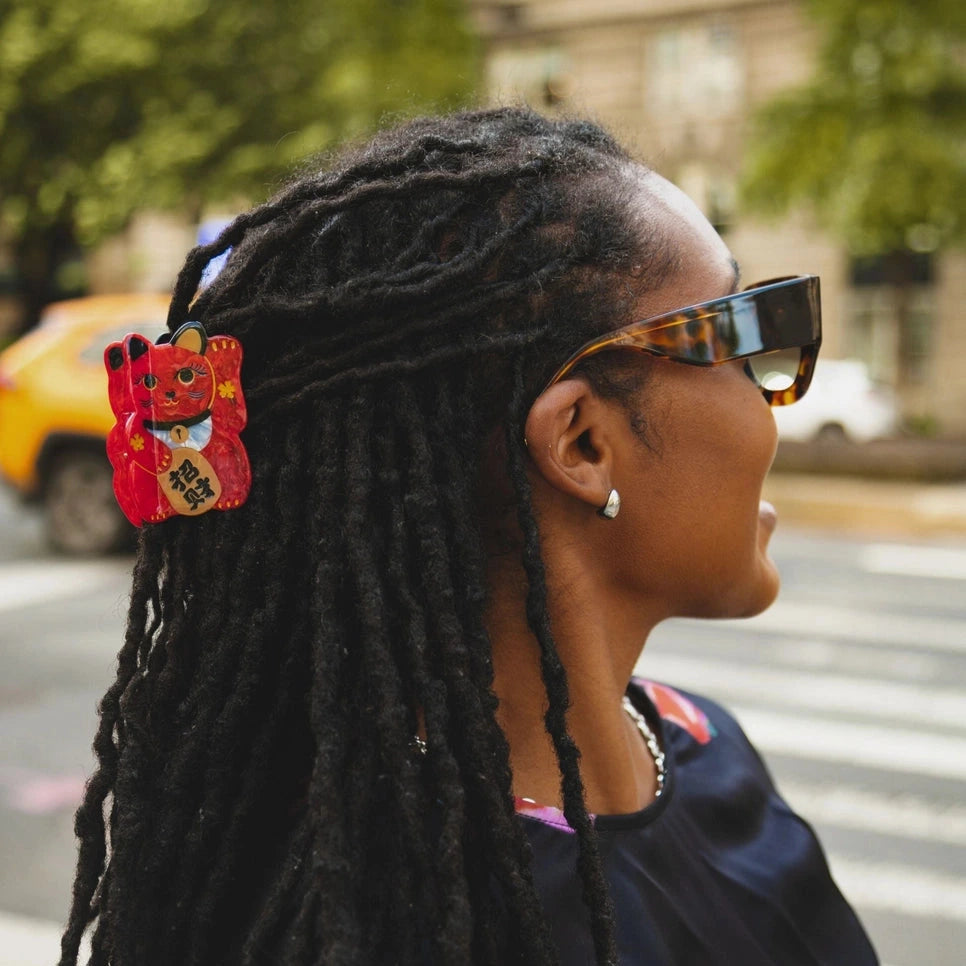 Person with braided hair wearing sunglasses and colorful earrings on a street.