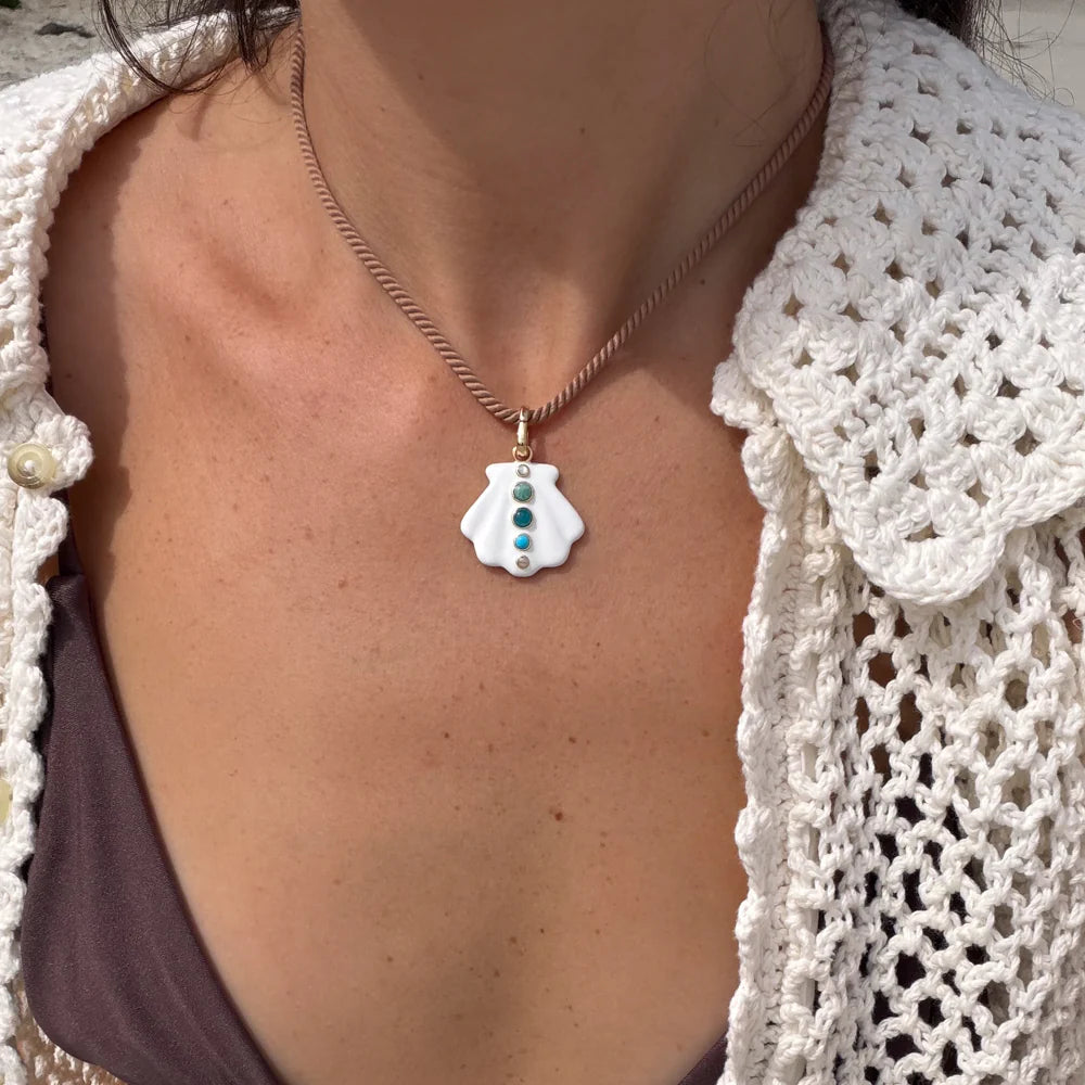 Person wearing a necklace with a shell pendant against a neutral background