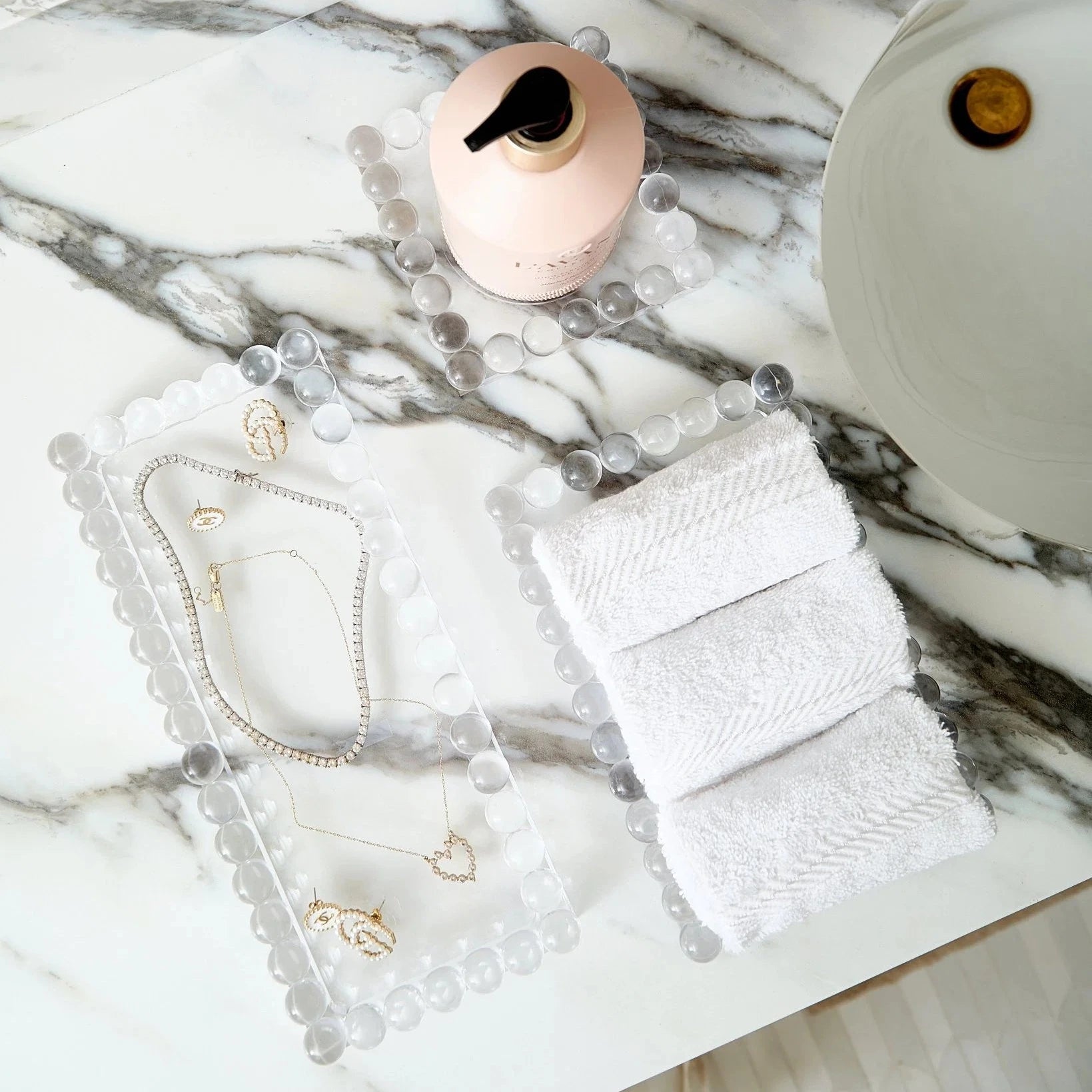 Jewelry set with a pink bottle and white towel on a marble surface