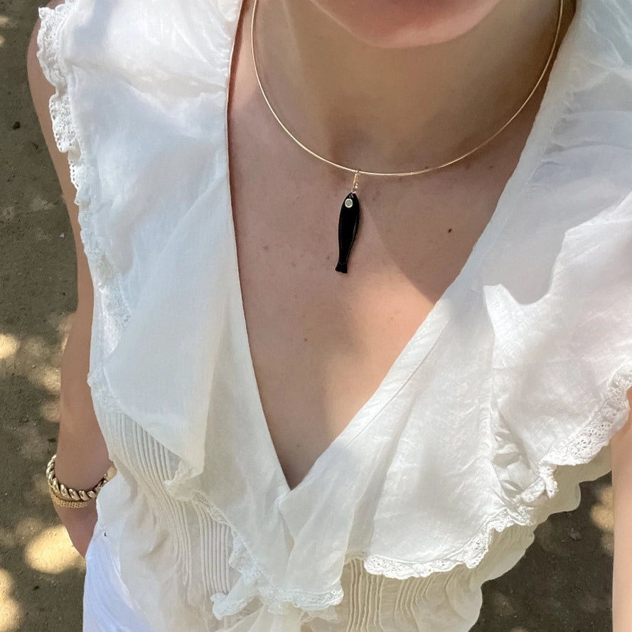 a gold choker necklace with a black fish charm worn with a white blouse