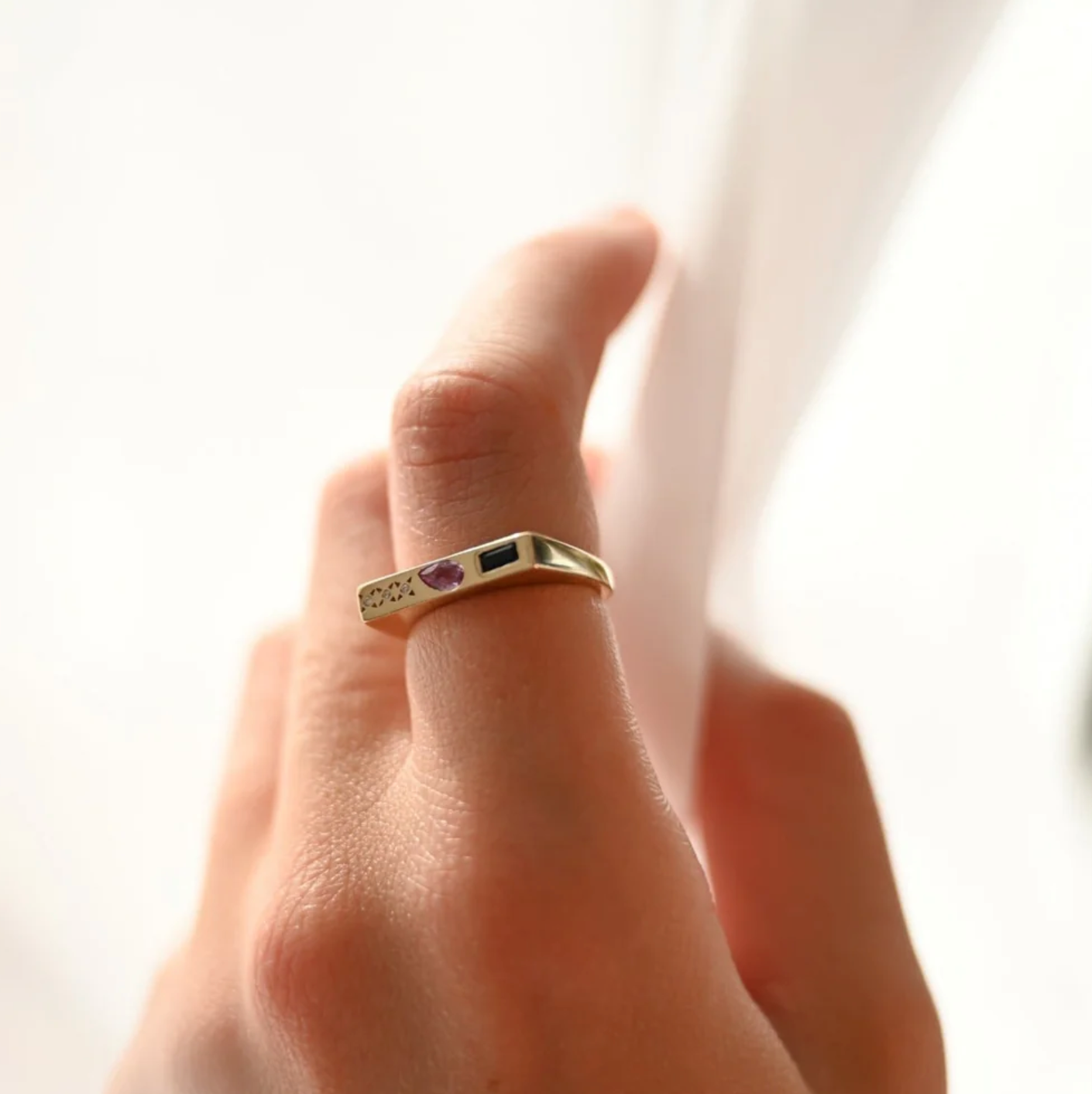 10k Gold ring with blue and pink gemstone on a person's finger against a white background