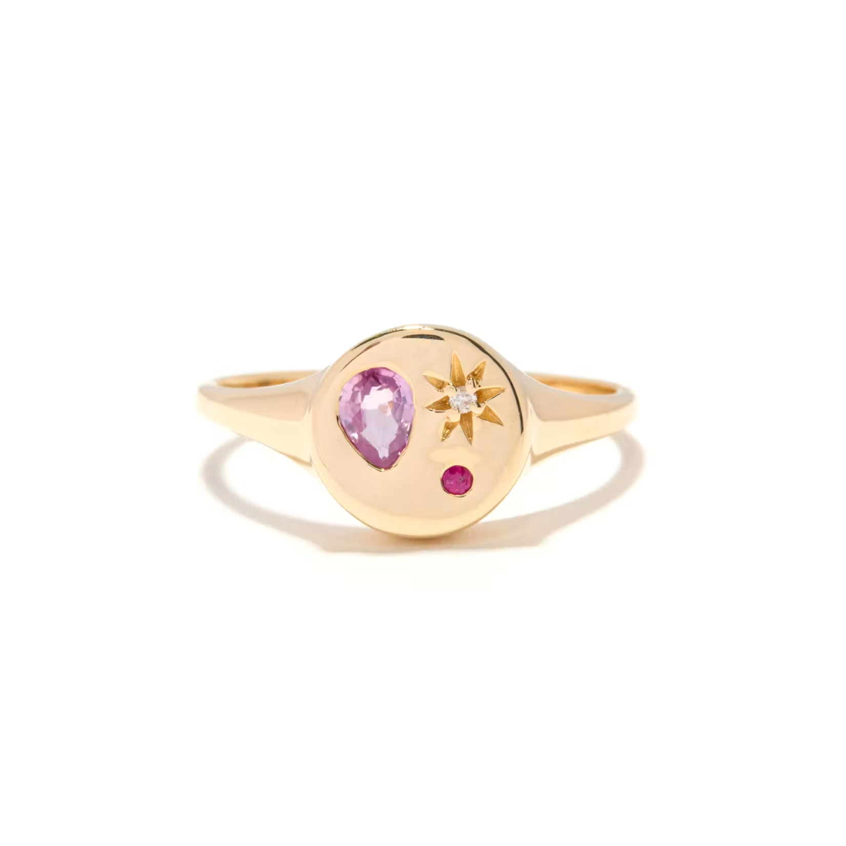 a gold signet ring with an inlay pink stone, red stone, and white stone with start motif over a white background