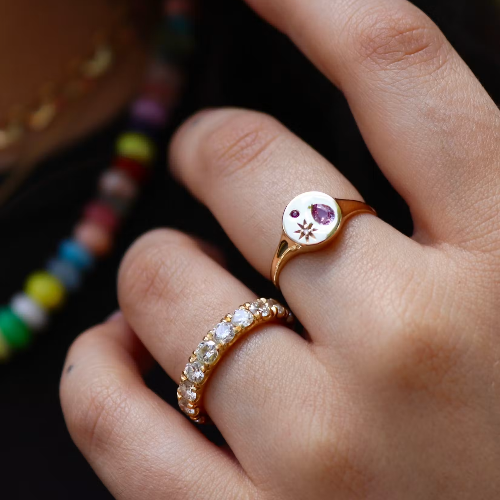 a persons hand wearing two gold rings over a black shirt and colorful necklaces
