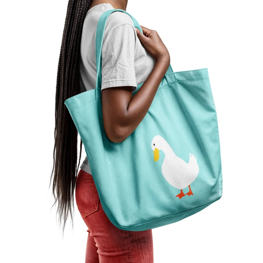 A woman wearing a white t-shirt and red jeans carries a light blue tote bag with a white duck graphic on the front, shown from a side-back angle against a solid white background.