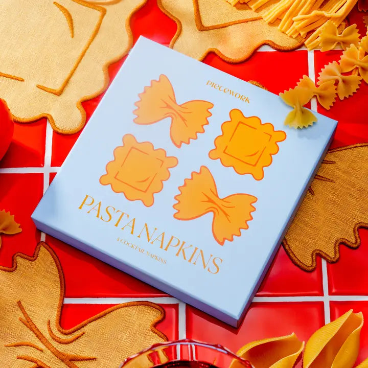 Blue box of pasta shaped cocktail napkins with a red background and pasta shaped cocktail napkins around