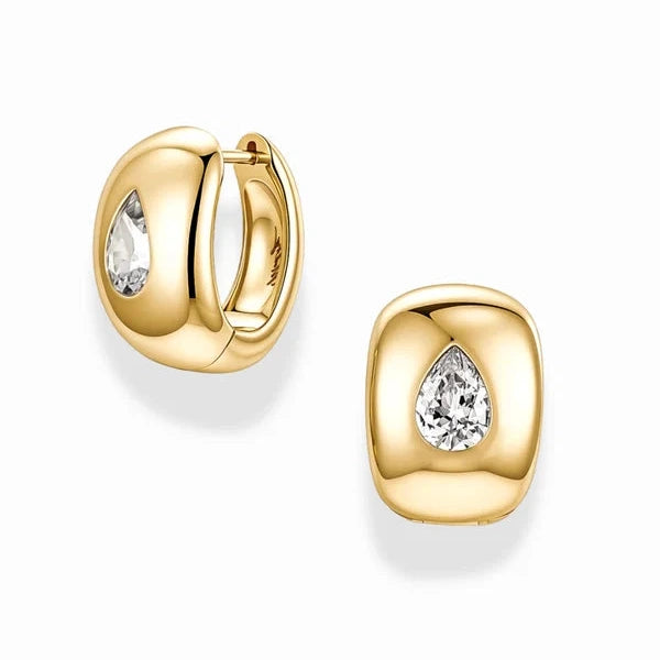 A pair of gold huggie hoop earrings, one shown from the front and the other from the side, both featuring a teardrop-shaped clear gemstone in a polished gold setting, on a white background.