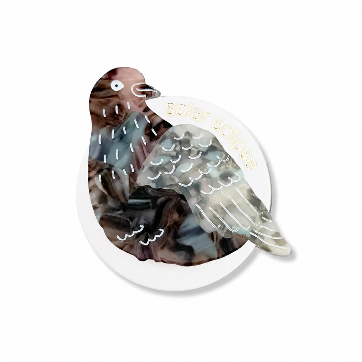 A circular acrylic pin featuring a stylized pigeon with a marbled brown, gray, and white pattern, with gold foil text reading 'solar eclipse' on a white background.