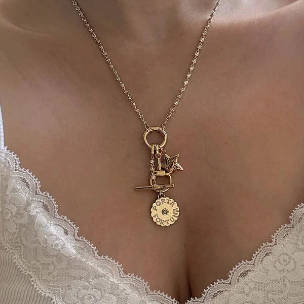 A gold-toned necklace with a small charm and a circular flower pendant, worn on a model's neck over a white lace-trim top.