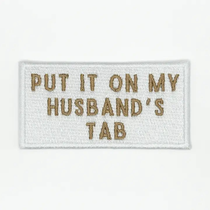 a white and gold patch with text reading put it on my husbands tab on a white background
